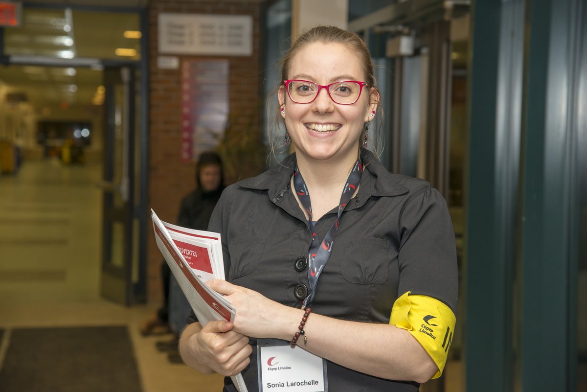 Employée souriante et accueillante avec feuillets dans les mains.