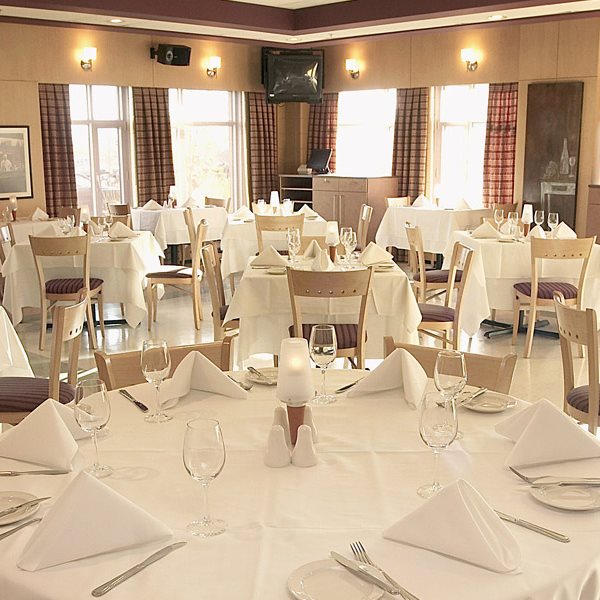 Tables de banquet avec nappes blanches, verres à vin, serviettes de table pliées. Lumière du jour qui perce à travers les fenêtres.