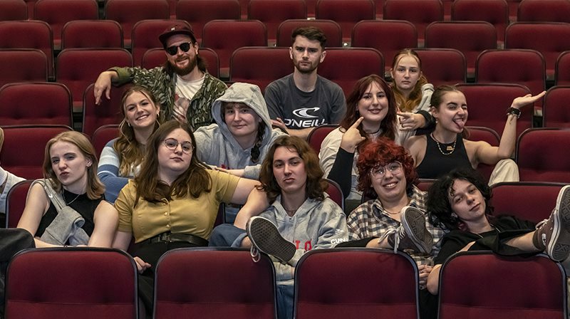 Les étudiants artistes de la troupe de théâtre du Grand escalier sont aussi dans la salle de spectacle et sourient à la caméra.