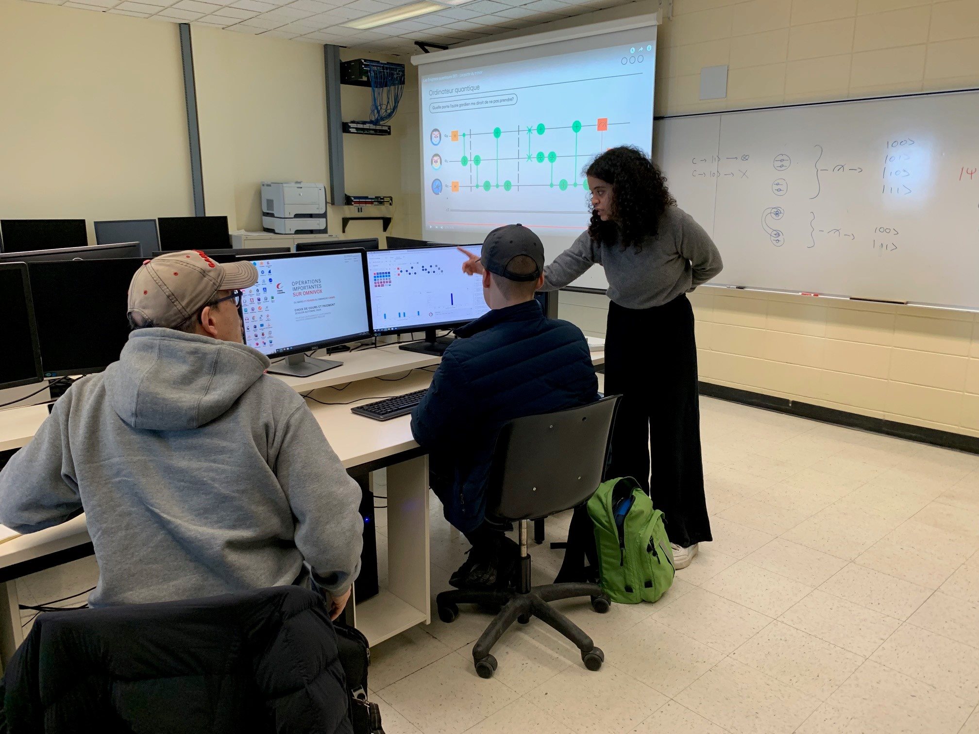 Des étudiants et étudiantes dans un laboratoire informatique, autour de deux écrans d'ordinateurs